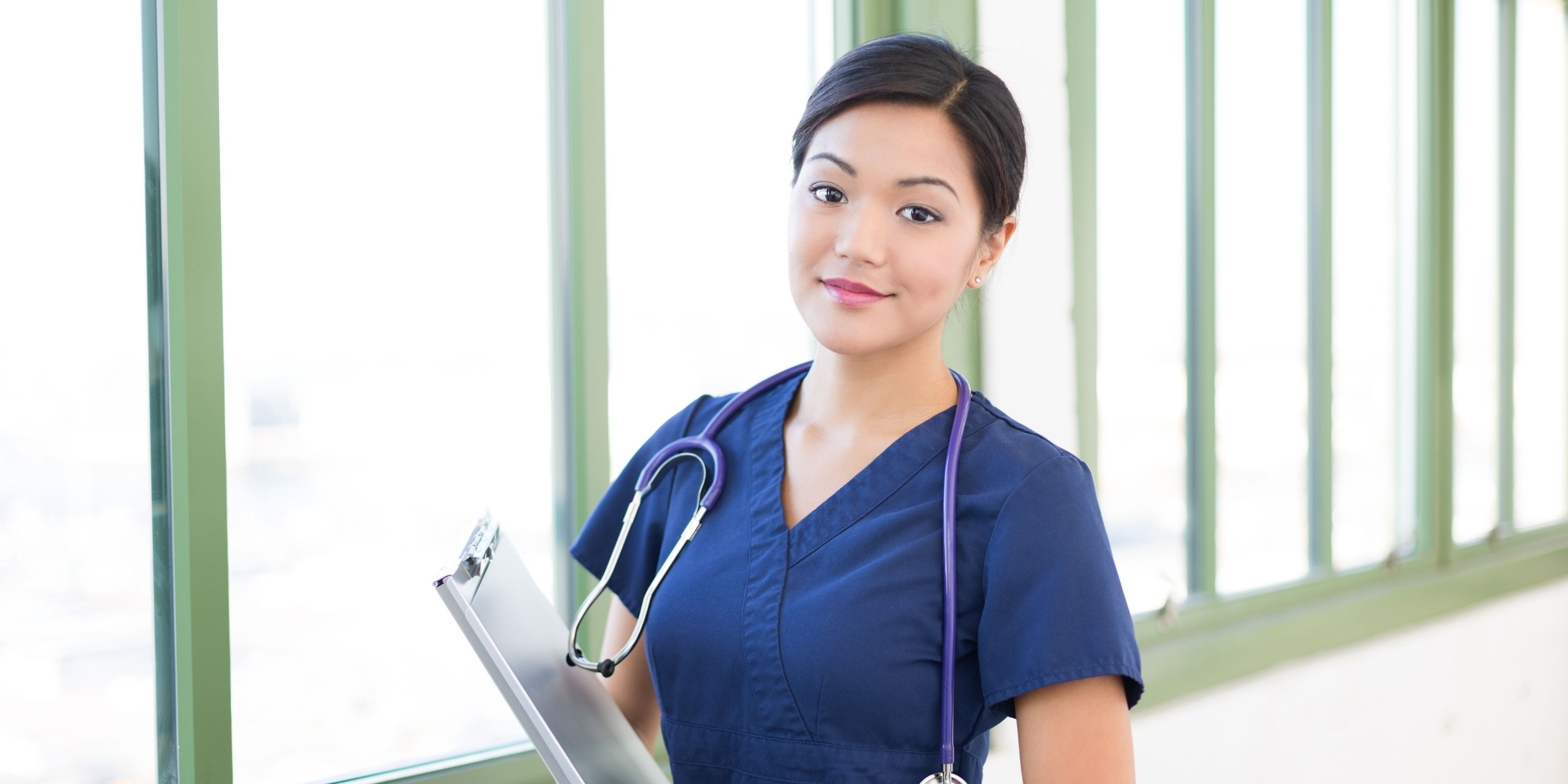 Confident female nurse wearing blue scrubs with a smile on her face, holding documents