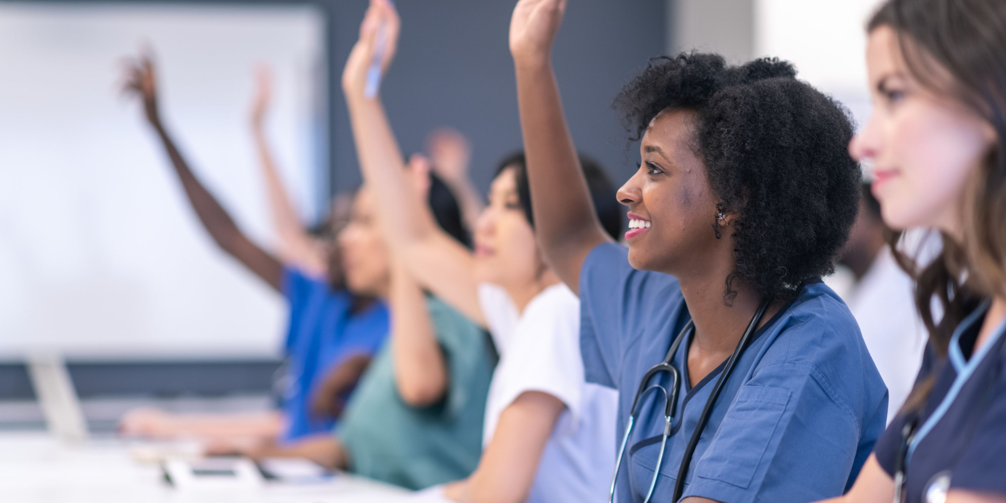 Nurses in class raising their hands to answer a questioned posed by their lecturer/teacher