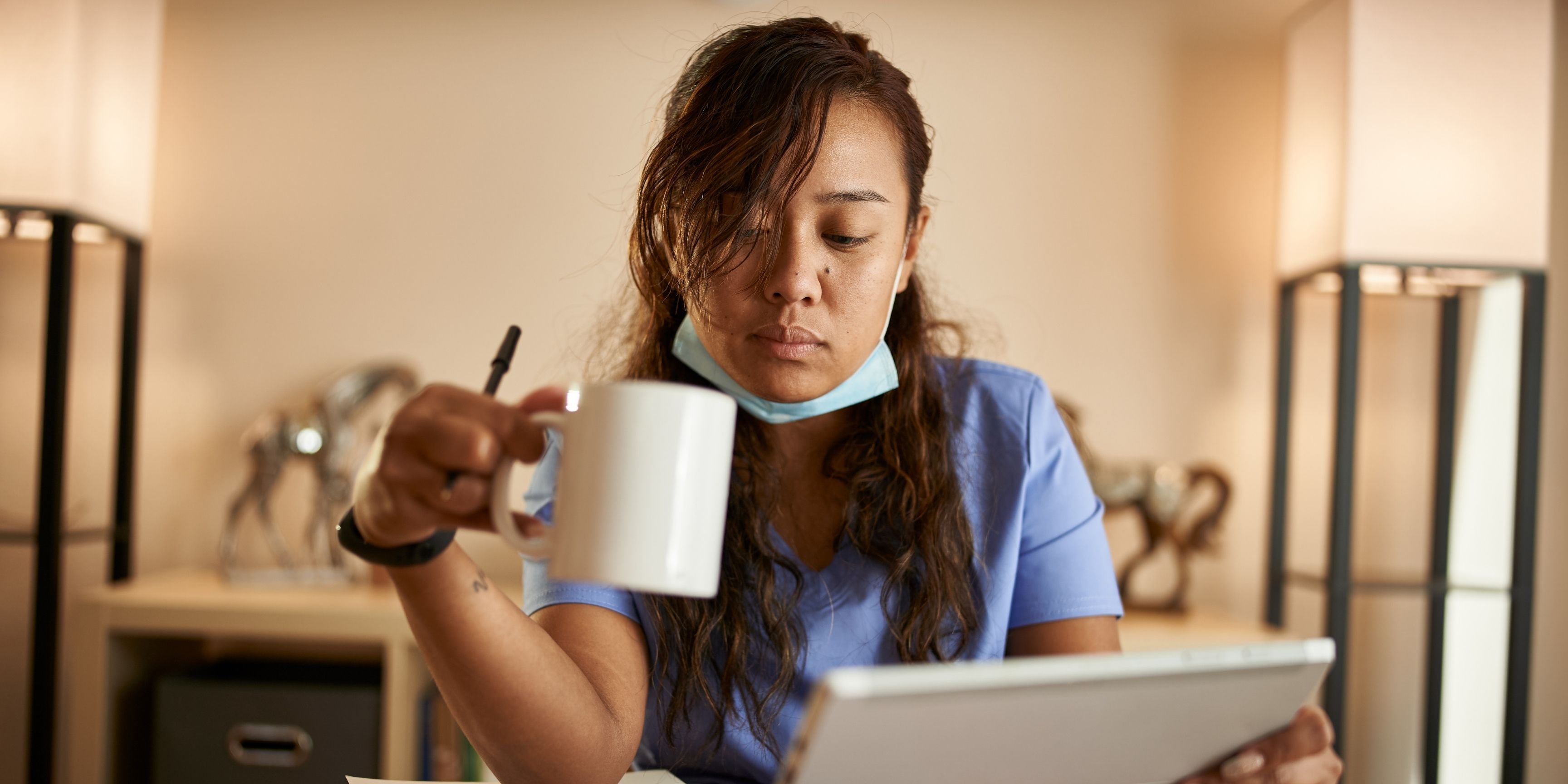 nurse drinking a cup of coffee while reviewing documents and compliance paperwork